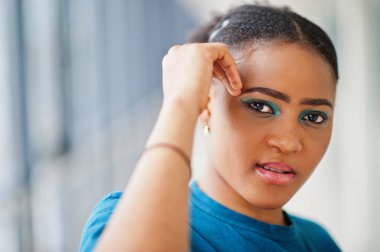 Mavi tişörtlü Afrikalı kadın içeride poz verdi.