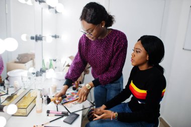 Afro-Amerikalı bir kadın güzellik salonunda makyaj sanatçısı tarafından makyaj yapıyor..