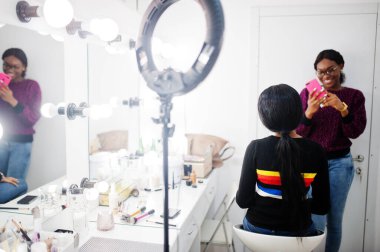 Afro-Amerikalı bir kadın güzellik salonunda makyaj sanatçısı tarafından makyaj yapıyor. Sanatçı çalışmalarının fotoğrafını cep telefonundan çekmiş..