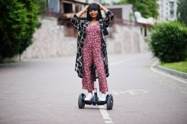Segway ya da uçan kaykay kullanan güzel bir Afro-Amerikan kadını. Çift tekerli siyah kız. Kendini dengede tutan elektrikli scooter..