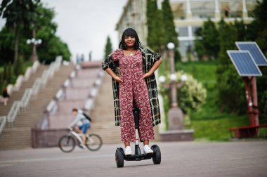 Segway ya da uçan kaykay kullanan güzel bir Afro-Amerikan kadını. Çift tekerli siyah kız. Kendini dengede tutan elektrikli scooter..
