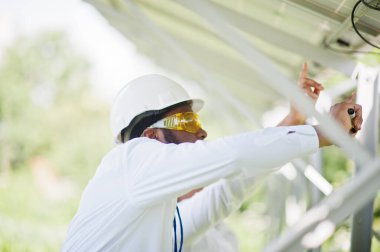 Afrikalı Amerikalı teknisyen güneş panellerinin bakımını kontrol ediyor. Üç siyah mühendis grubu güneş istasyonunda buluşuyor..
