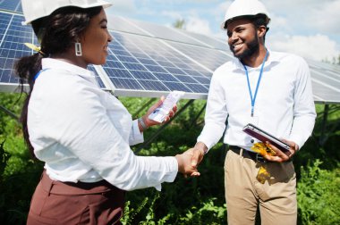 Afrikalı Amerikalı teknisyen güneş panellerinin bakımını kontrol ediyor. Üç siyah mühendis grubu güneş istasyonunda buluşacak ve parayla bir anlaşma yapacaklar..