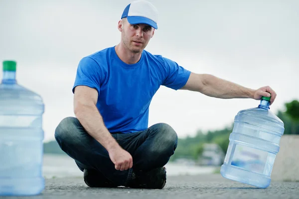 Delivery man sitting with water bottles outdoor.