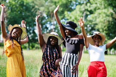 Dört muhteşem Afro-Amerikalı kadın grubu yeşil çimlerde vakit geçirmek için yaz şapkası takıyor..