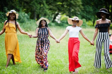 Dört muhteşem Afro-Amerikalı kadın grubu yeşil çimlerde vakit geçirmek için yaz şapkası takıyor..
