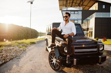 Beyaz gömlekli ve güneş gözlüklü katı Asyalı adam siyah mafya arabasının yanında poz vermiş.. 