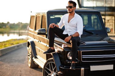 Beyaz gömlekli ve güneş gözlüklü katı Asyalı adam siyah mafya arabasının yanında poz vermiş.. 