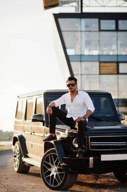 Beyaz gömlekli ve güneş gözlüklü katı Asyalı adam siyah mafya arabasının yanında poz vermiş.. 