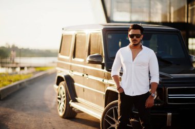 Beyaz gömlekli ve güneş gözlüklü katı Asyalı adam siyah mafya arabasının yanında poz vermiş.. 