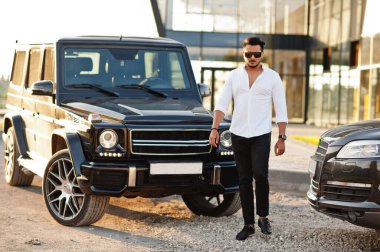 Beyaz gömlekli ve güneş gözlüklü katı Asyalı adam siyah mafya arabalarının yanında poz vermiş..