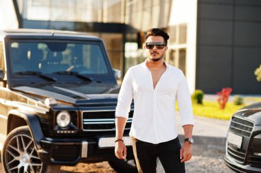 Beyaz gömlekli ve güneş gözlüklü katı Asyalı adam siyah mafya arabalarının yanında poz vermiş..