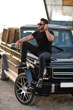 Asyalı adam arazi aracının yanında siyah poz vermiş..