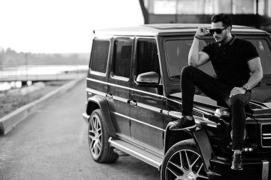 Asyalı adam arazi aracının yanında siyah poz vermiş..