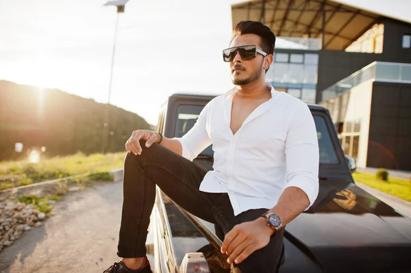 Solid asian man in white shirt and sunglasses posed near black mafia suv car.