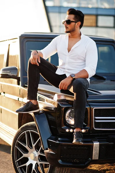 Beyaz gömlekli ve güneş gözlüklü katı Asyalı adam siyah mafya arabasının yanında poz vermiş.. 