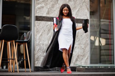 Diplomalı genç Afro-Amerikan öğrenci açık havada poz veriyor.