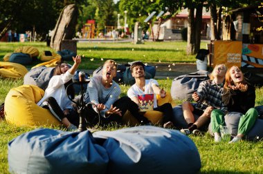 Genç çoklu etnik gruptan insanlar puf diye film izleyip açık hava sinemasında patlamış mısır fırlatıyorlar..