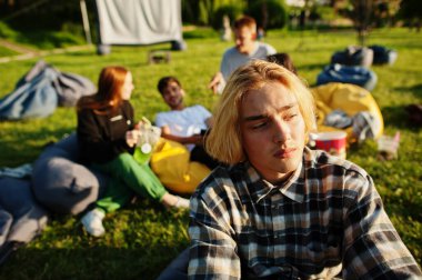 Açık hava sinemasında film izleyen çok ırklı bir grup genç. Komik adamın yakın portresi..