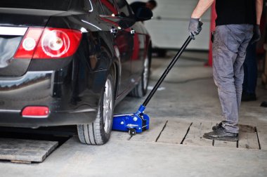 Araba tamiri ve bakım teması. Otomobil servisinde çalışan tamirci. Tamir için hidrolik zemin krikosuyla kaldırılmış..