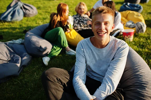 Young multi ethnic group of people watching movie at poof in open air cinema. Close up portrait of funny guy.