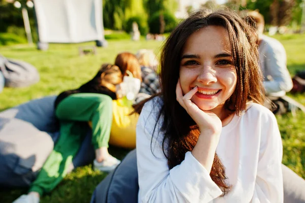 Young multi ethnic group of people watching movie at poof in open air cinema. Close up portrait of funny girl.