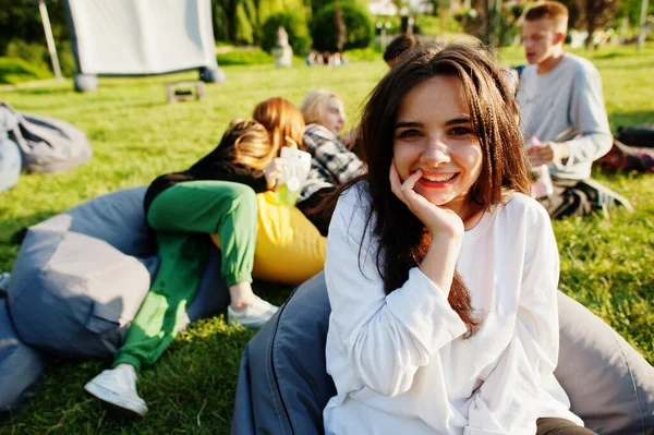 Young multi ethnic group of people watching movie at poof in open air cinema. Close up portrait of funny girl.