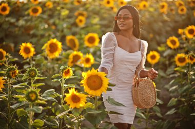 Güzel siyah kadın ayçiçeği tarlasında yaz elbisesi giymiş..