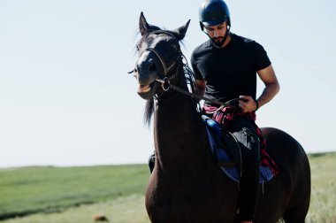Arap uzun sakallı adam siyah kask takıyor, Arap atına biniyor..