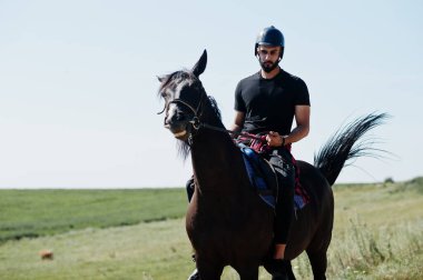 Arap uzun sakallı adam siyah kask takıyor, Arap atına biniyor..