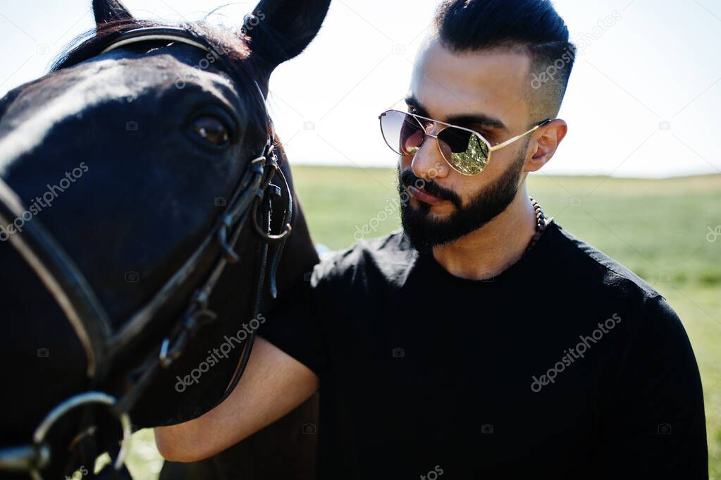 Arab tall beard man wear in black and sunglasses with arabian horse.