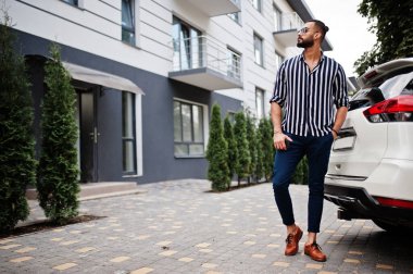 Başarılı bir Arap, çizgili gömlek ve güneş gözlüğü takıyor ve beyaz arazi aracının yanında poz veriyor. Tarz sahibi Arap erkekleri nakliye işinde.