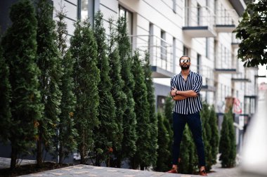 Başarılı bir Arap erkeği çizgili gömlek ve güneş gözlüğü takıyor..