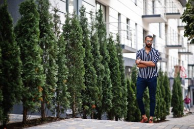 Başarılı bir Arap erkeği çizgili gömlek ve güneş gözlüğü takıyor..