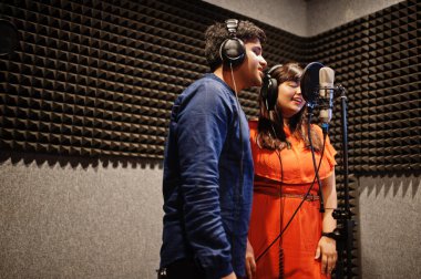 Young asian duet singers with microphone recording song in record music studio. clipart