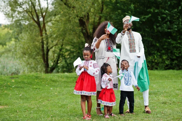 African family in traditional clothes with nigerian flags at park.