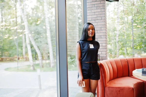 Fashionable feminist african american woman wear in black t-shirt and shorts, posed at restaurant.