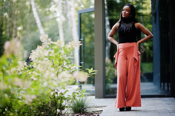 Fashionable african american woman in peach pants and black blouse pose outdoor.