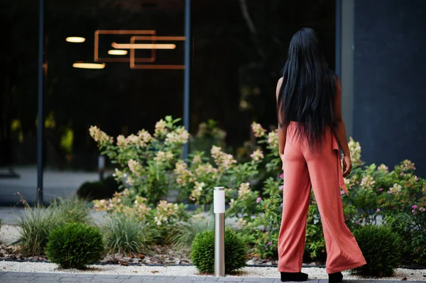 Fashionable african american woman in peach pants and black blouse pose outdoor.