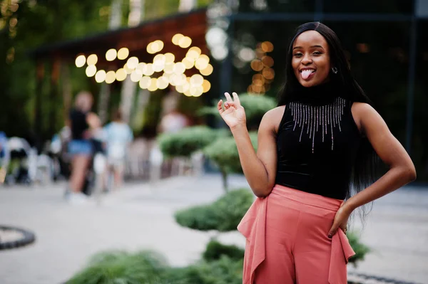 Fashionable african american woman in peach pants and black blouse pose outdoor.