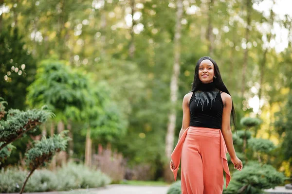 Fashionable african american woman in peach pants and black blouse pose outdoor.