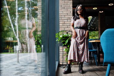 Uzun elbiseli, çizmeli ve gözlüklü Afro-Amerikan kadının moda portresi..