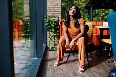 Güzel siyah kadın portresi, turuncu kıyafetler giyin, restoranda poz ver..