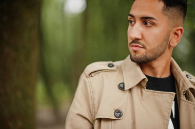 Trençkot giymiş şık bir Kuveytli parkta yürüyor..