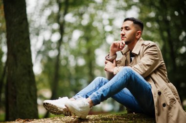 Trençkottaki şık Kuveytli adam ağaçta, ağaçta oturuyor..