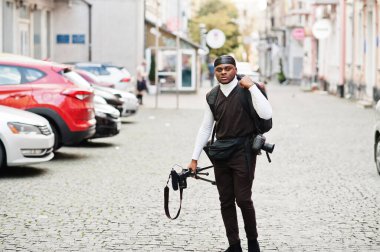 Genç, Afro-Amerikan kameraman tripod profesyonel ekipmanla profesyonel kamera tutuyor. Siyah Duraq giyen Afro kameraman video çekiyor.