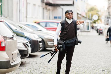 Genç, Afro-Amerikan kameraman tripod profesyonel ekipmanla profesyonel kamera tutuyor. Siyah Duraq giyen Afro kameraman video çekiyor.