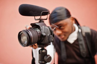 Profesyonel Afrikalı Amerikalı genç kameraman profesyonel ekipmanlarla profesyonel kamera tutuyor. Siyah Duraq giyen Afro kameraman video çekiyor.