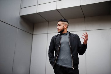 Tarz sahibi Arap sakallı adamın portresi gri balıkçı yaka ve siyah jaket giyiyor. Çelik duvara karşı Arap model adam..