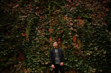 Tarz sahibi Arap sakallı adamın portresi gri balıkçı yaka ve siyah jaket giyiyor. Sonbahar yapraklarının arka planındaki Arap model adam..